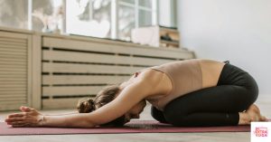Woman on yoga mat in child's pose at home. This article shares a simple 5 minute yoga flow.