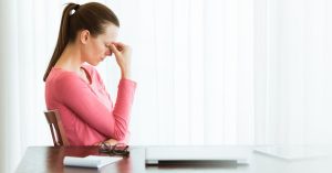 Woman sitting at table with head down. This articles discusses how to stop stressing about everything.