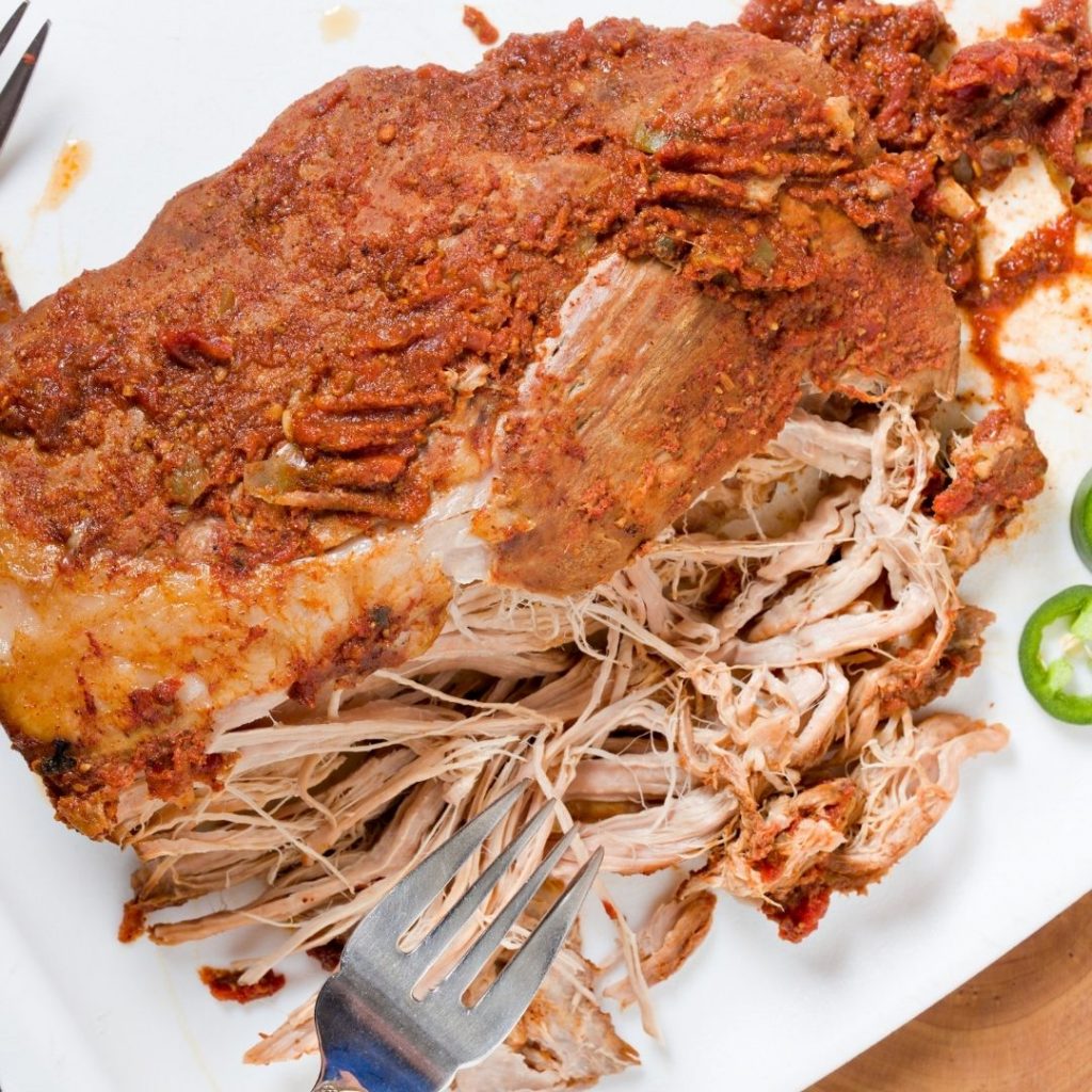 Paleo slow cooker pulled pork on a white plate with a fork pulling it apart.