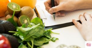 Person writing diet plan next to healthy foods. This post is about creating a hormonal imbalance diet plan.