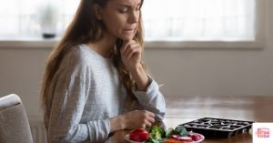 Woman with salad and chocolate in front of her. This article discusses important mindful eating questions to reflect on.