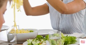 Salad on a counter with a person in background taking pasta out of a bowl. This articles discusses three mindful eating habits.