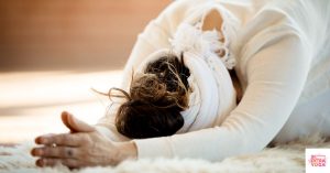 Woman doing yoga on white carpet in child's pose. This article discusses yoga and hormones.