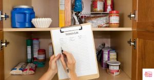 Person holding clipboard and looking in cupboard making a grocery list. This article share a free anti-inflammatory diet food list pdf.