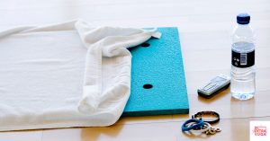 Towel over an exercise mat with a phone and water bottles next to it. This article discusses the best yoga towels.