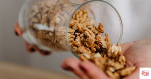 A person pouring walnuts from a glass jar into her hand. This article discusses the best elimination diet snacks.