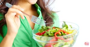 Woman eating a salad in a glass bowl. This article is about the elimination diet and how long it takes to see results.