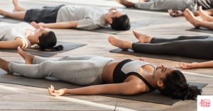 People doing corpse pose in yoga class. This article discusses Ashtanga vs vinyasa yoga.