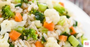 Cooked broccoli, cauliflower, carrots, and rice on a white plate. This article discusses eating cruciferous vegetables for hormone balance.