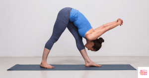 Woman bending over with feet apart on a yoga mat. This articles asks: Is vinyasa yoga hard?