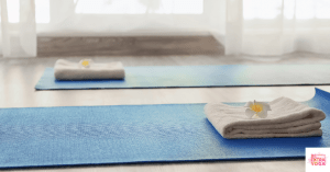 Blue yoga mats on floor with folded towel on top of each one. This article discusses a yoga mat vs a yoga towel.