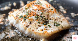 Flaky white fish cooking in a frying pan. This article shares a paleo halibut recipe.
