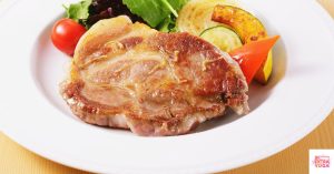 Pork chop on a white plate with salad. This article shares a recipe for paleo pork chops.