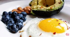 Sunny side up egg with blueberries, avocado, and nuts on a white plate. This article discusses ideas for hormone balancing breakfast.
