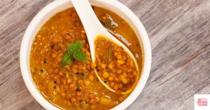 Aerial view of lentil soup in white bowl sitting on wooden table. This article shares hormone balancing lunch ideas.
