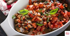 Chopped tomatoes and basil over baked chicken in a white bowl. This article shares a recipe for paleo bruschetta chicken.