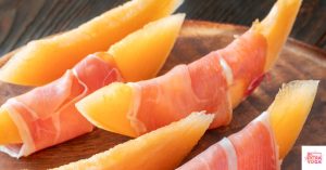 Prosciutto-wrapped mangos on a circular wooden tray. This articles shares a recipe for paleo prosciutto-wrapped mango.